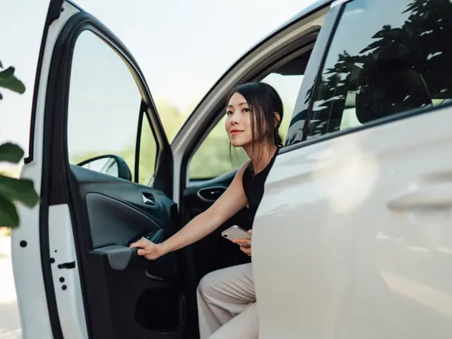 Mujer joven saliendo del asiento del conductor de un monovolumen blanco.
