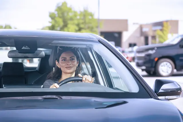 Una mujer detrás del volante de un sedán azul saliendo de un estacionamiento.